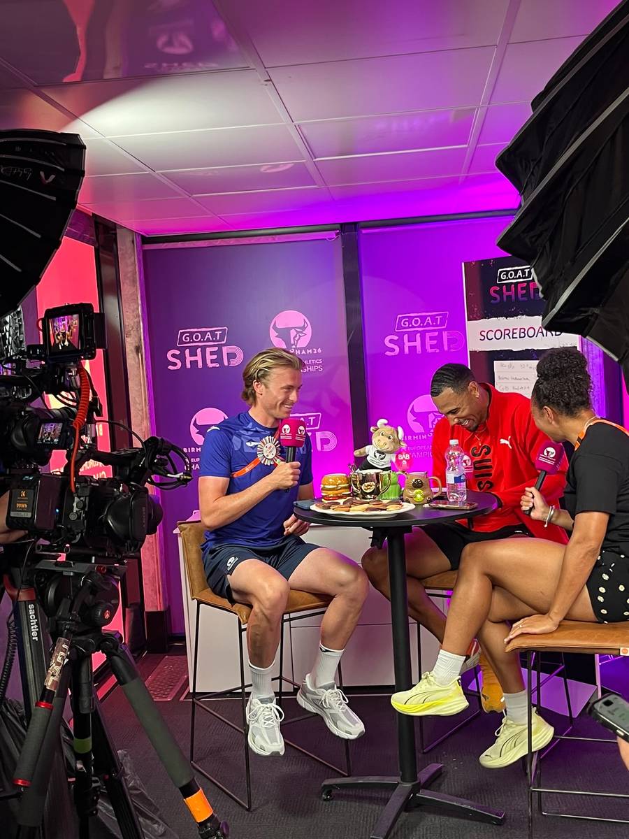 A medallist laughing in the GOAT Shed, with the quiz scoreboard behind